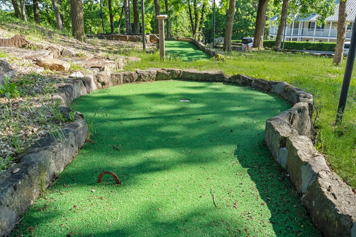 A charming mini-golf course set amidst lush landscaping and a winding stone pathway. The inviting scene hints at joyful family gatherings and friendly competition, with greenery providing a relaxed backdrop.