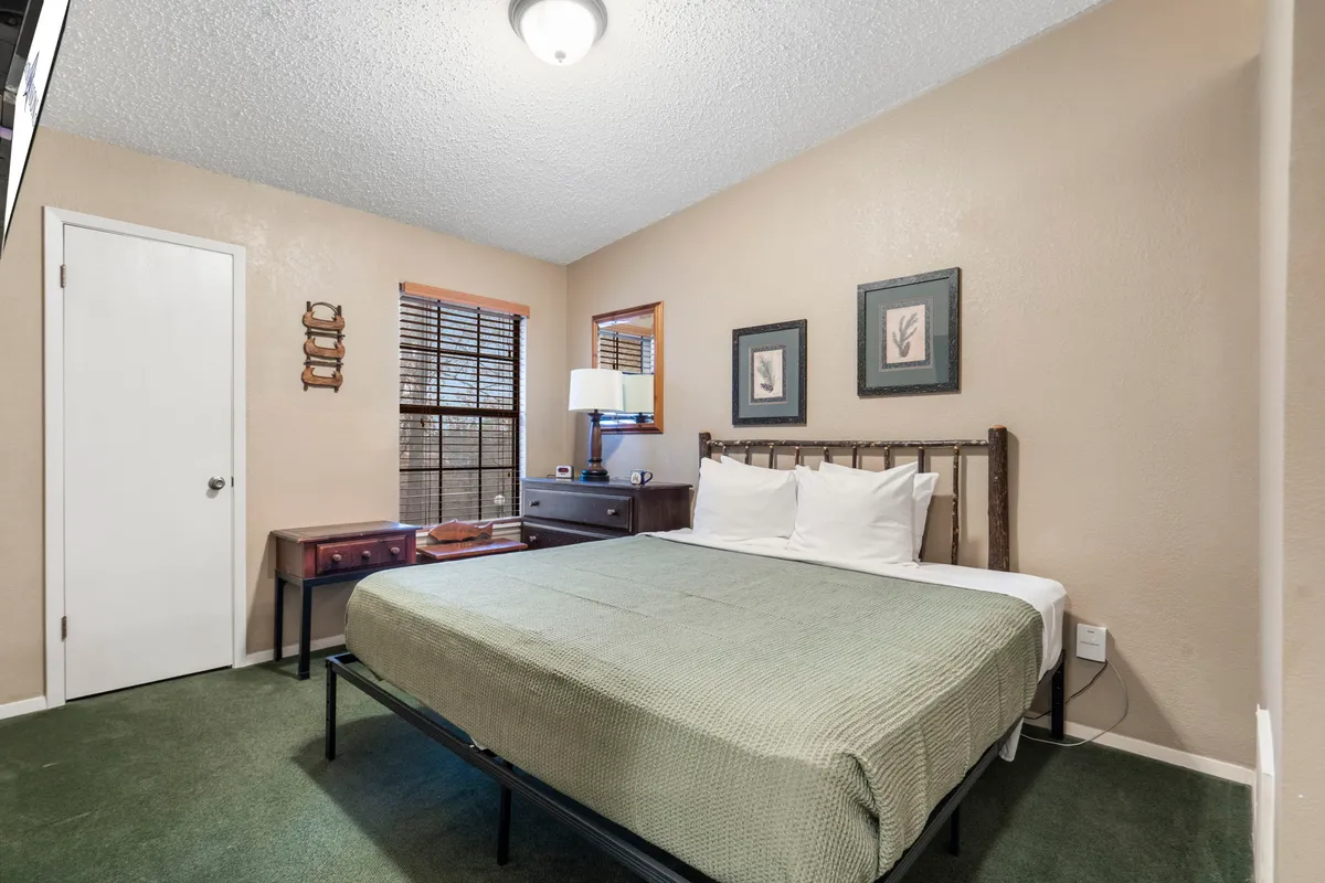 A cozy bedroom featuring a plush bed, nightstand, lamp, and framed pictures. The soft lighting and inviting decor create a warm, restful atmosphere ideal for relaxation and peaceful sleep.