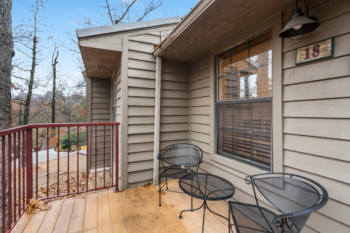 A tranquil private balcony with black metal chairs arranged on a wooden deck, offering views through a window to the outdoors. The serene setup invites relaxation, perfect for enjoying coffee or pastries while taking in the surrounding natural beauty and fresh air.