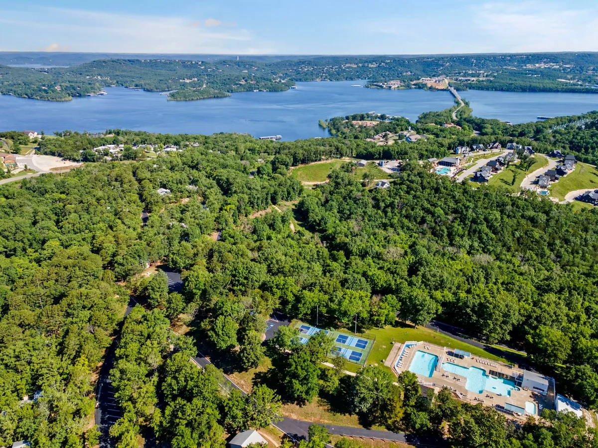 A wide view of a lake bordered by a swimming pool, tennis courts, and lush greenery, capturing the activity and community spirit of the area. The open landscape invokes a sense of freedom and exploration, perfect for family and pet outings.