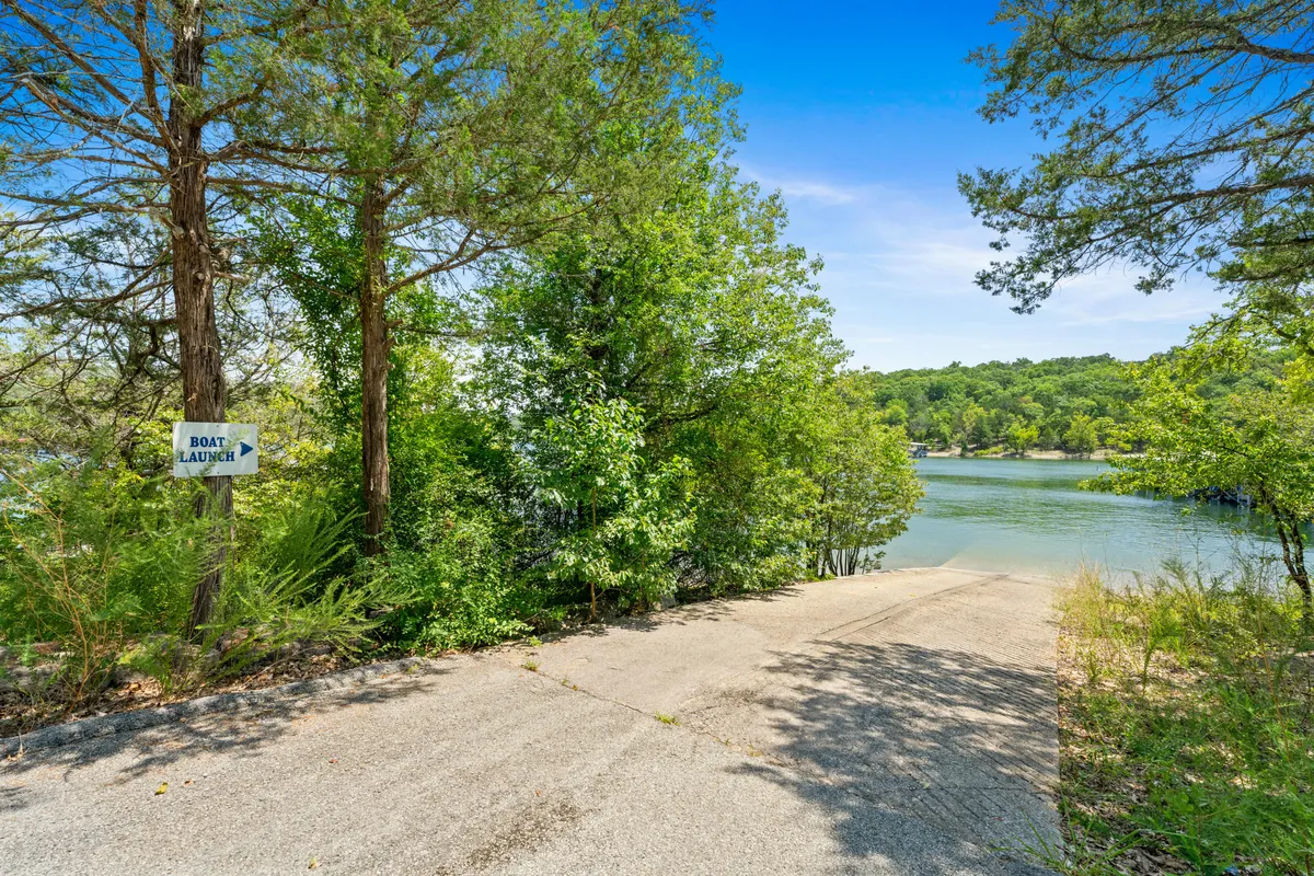 A peaceful exterior shot featuring a boat launch sign, a clear waterway ready for boating or fishing, and mature trees framing the scene. The atmosphere suggests quiet mornings spent launching kayaks or preparing for a day on the water.