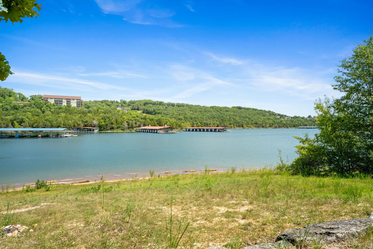 A peaceful lakeside view with docks extending into the water, green rolling hills in the background, and a soft sky overhead. The mood is calm and intimate, inviting guests to stroll along the shore, savor sunsets, or simply reflect by the water.