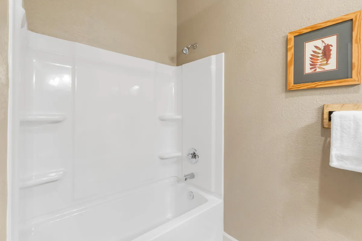 A serene bathroom scene with a bathtub, framed artwork, towel rack, and neatly hung towel. The calming design suggests a perfect spot for unwinding with a soothing bath or refreshing shower.